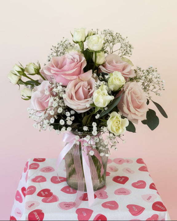 Pink arrangement with 6 roses, mini roses, baby’s breath, and greenery in a glass vase